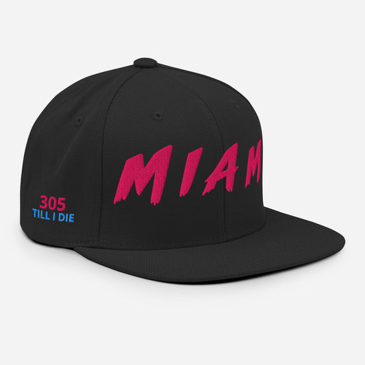 A black flat-brim snapback cap featuring a large pink 'MIAM' graphic on the front and '305 TILL I DIE' in pink and blue on the side, shown on a light gray background.