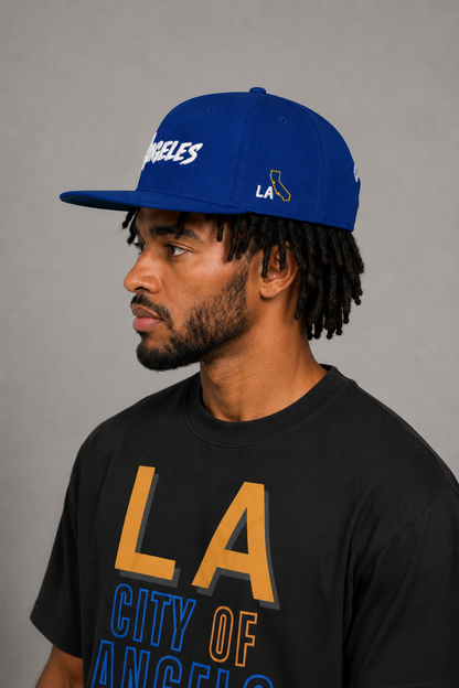 Los Angeles City of Angels Royal Blue Embroidered Snapback Hat — close-up model profile showing gold California state outline and white LA side embroidery | City 2 City Wear